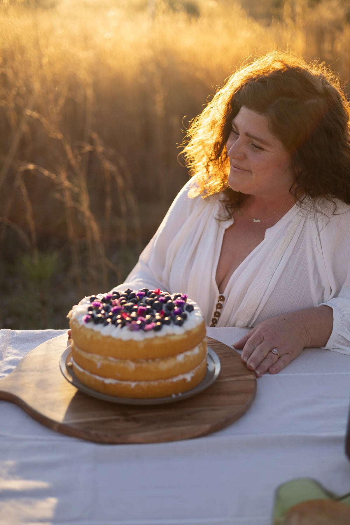 Woman sitting at a table with a cake outdoors during sunset